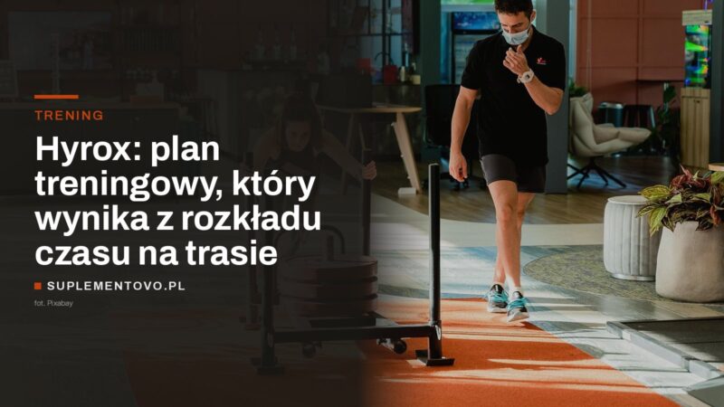 Zawodniczka pcha obciążone sanki treningowe po podłodze siłowni, obok idzie trener