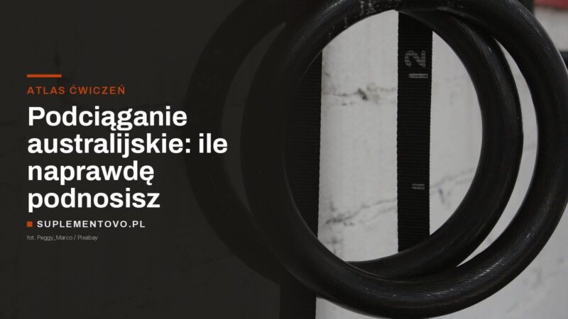 Kółka gimnastyczne zawieszone na taśmach przy białej ceglanej ścianie siłowni
