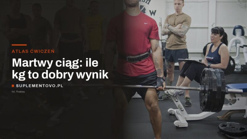Zawodnik w pasie treningowym kończy martwy ciąg sztangą obciążoną krążkami, obok sędzia z protokołem